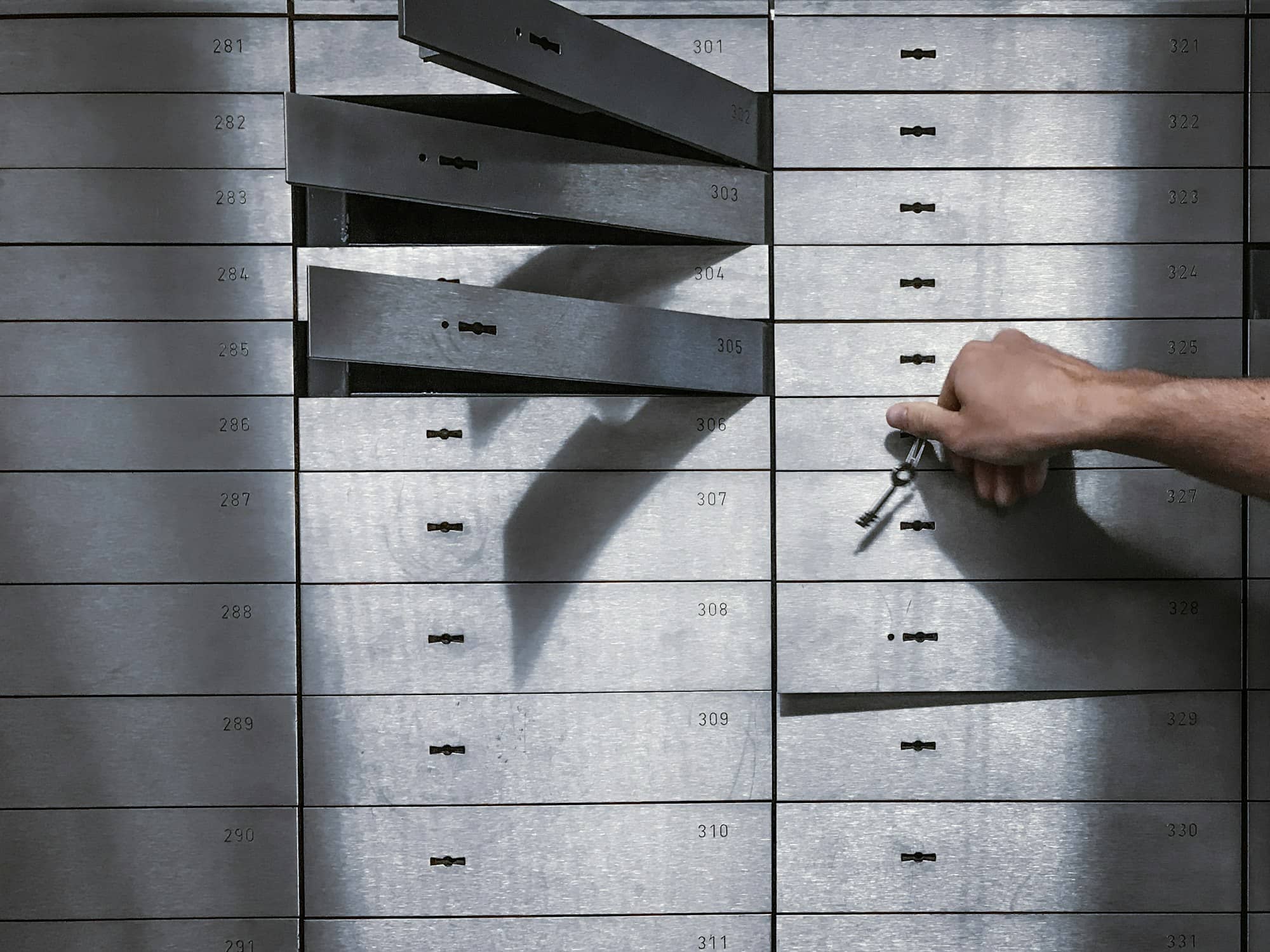 A hand turning a key in one of a wall of numbered deposit boxes